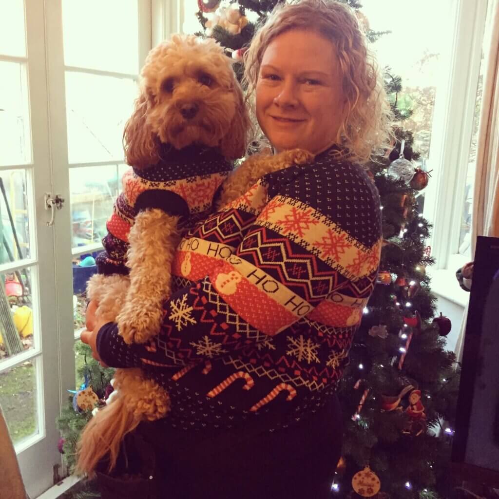 Carrie + Eric indoors – “Carrie smiling and holding Eric the Cavapoo, now a calm and confident helper dog”